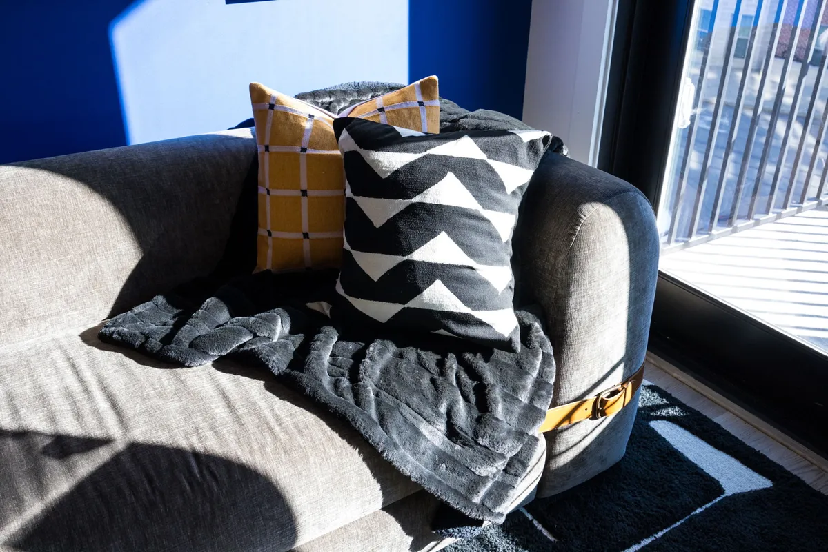 A cozy living area showcasing a plush couch with colorful pillows and a textured blanket, positioned beside a window that fills the space with natural light—suggesting a comfortable spot for reading or relaxing.