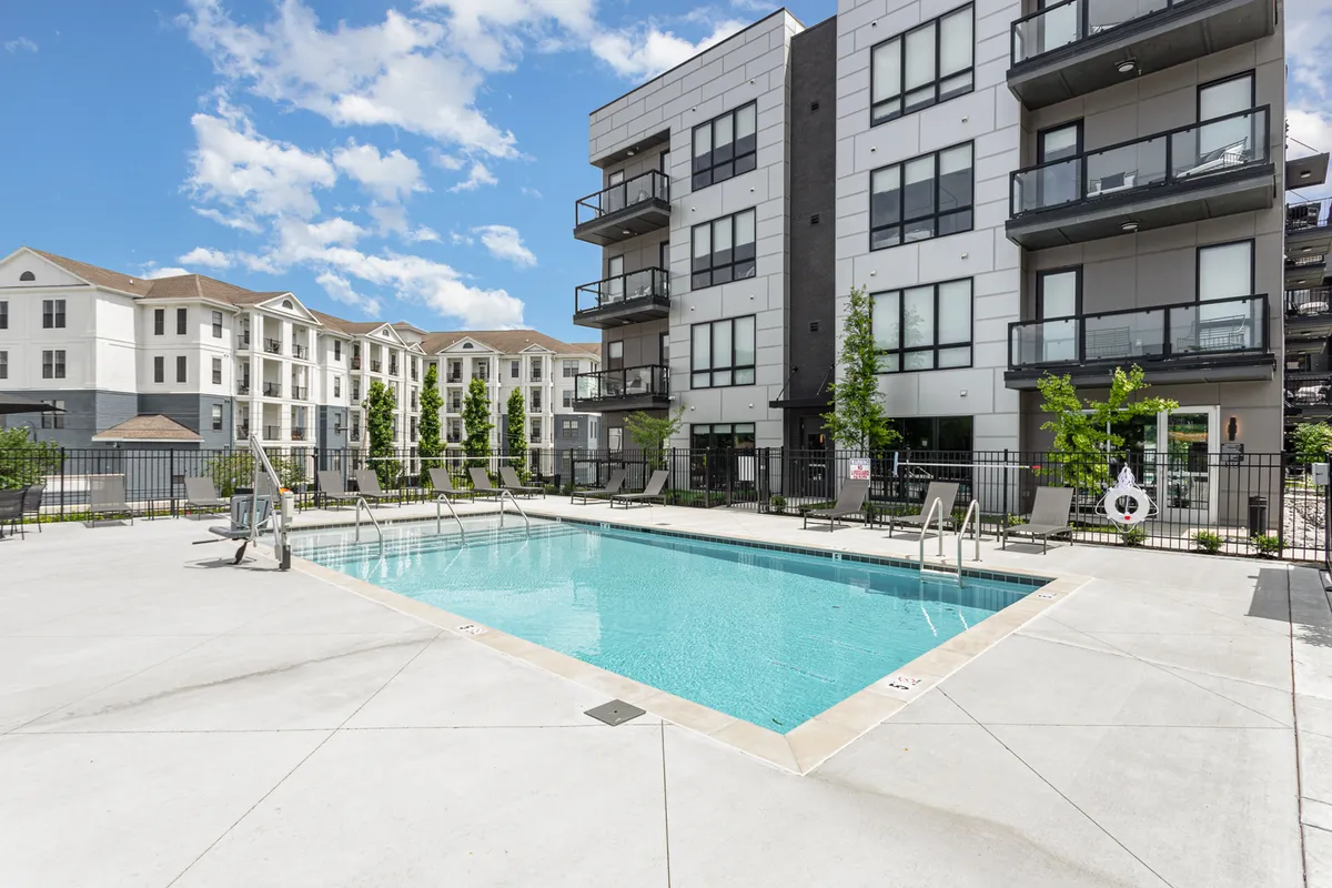 This image features a sparkling swimming pool surrounded by inviting balconies and landscaped greenery. The area is set against the backdrop of surrounding buildings, creating a luxurious oasis feel within the urban environment. Sun loungers and communal spaces around the pool suggest opportunities for social gatherings and relaxation.