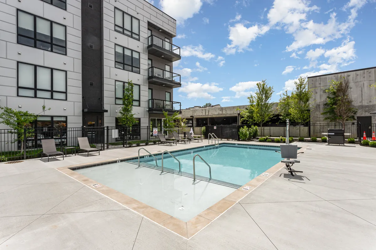 An inviting outdoor swimming pool surrounded by greenery, with balconies of the building visible. Sunlight glints off the water, and the area is set up for relaxation, socializing, and group gatherings, capturing the spirit of shared amenities at the property.