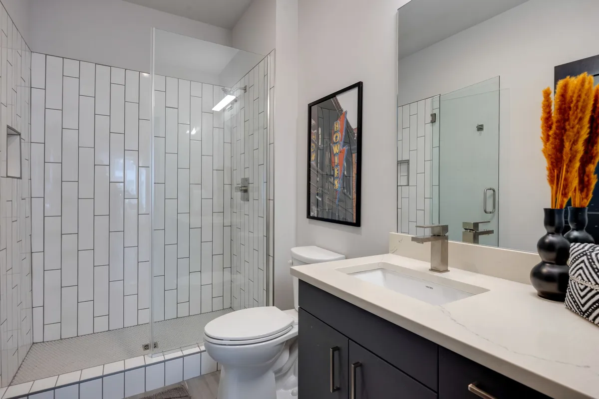 A stylish, fresh bathroom with a glass shower enclosure, floating vanity, modern fixtures, a decorative vase with dried plants, and framed artwork, radiating a spa-inspired ambiance.