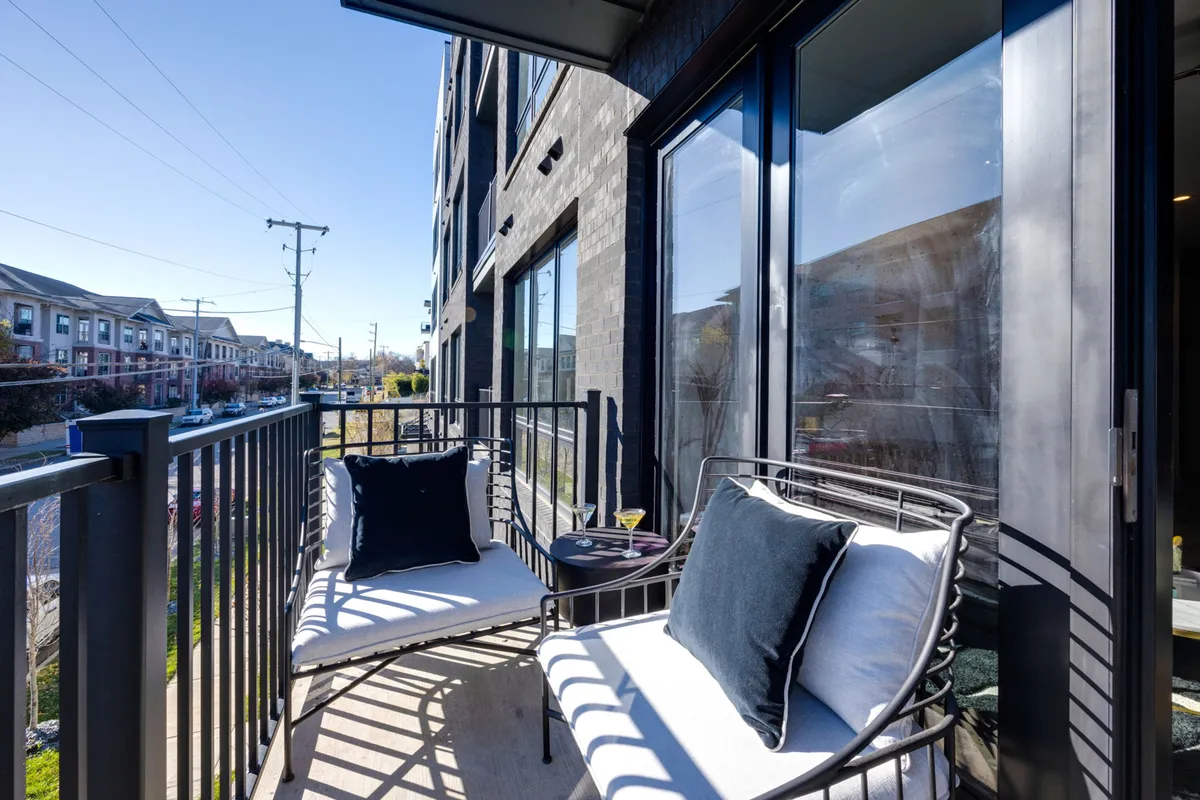 A cozy private balcony furnished with inviting seating, decorative pillows, and a small table, overlooking the city. The setting is ideal for enjoying morning coffee, reading, or intimate social gatherings, with a tranquil urban backdrop.