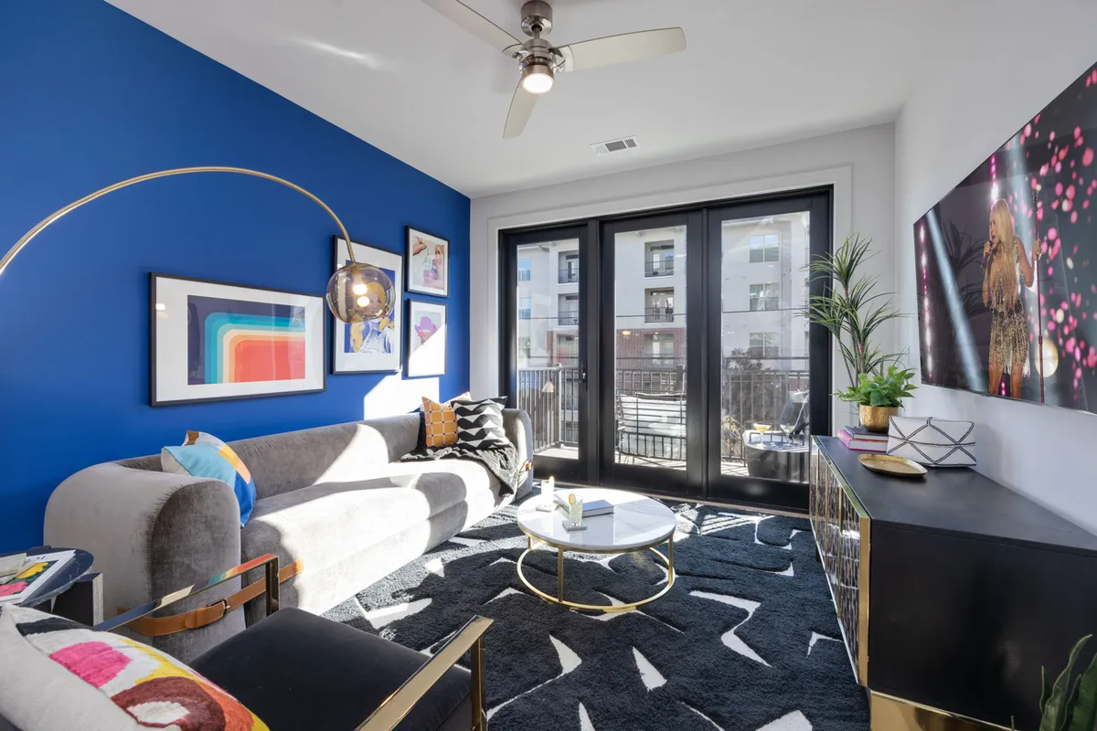 A bright and stylish living area featuring a blue accent wall adorned with modern artwork, a sleek coffee table, and a contemporary couch. Natural light streams in, creating a welcoming space perfect for relaxing, entertaining guests, or enjoying a morning coffee.